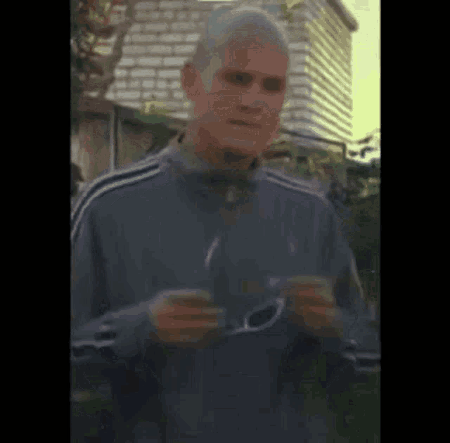 a man in a gray jacket is holding a pair of sunglasses in his hands .