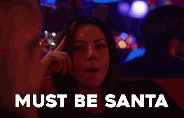 a woman is sitting in a dark room with the words must be santa behind her