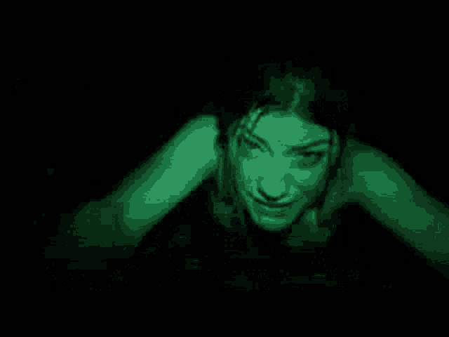 a woman is crawling in the dark with a green light coming out of her eyes .
