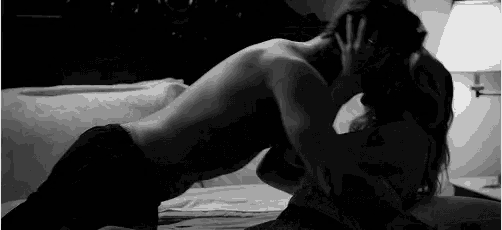 a black and white photo of a man and a woman kissing on a bed .