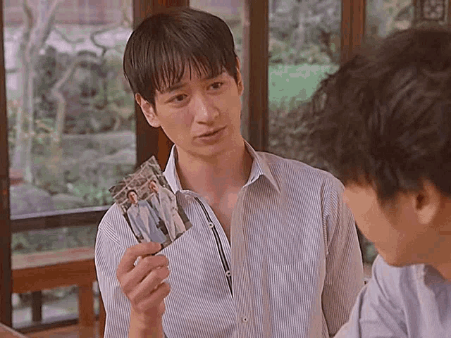 a man in a striped shirt is holding a picture of two men .