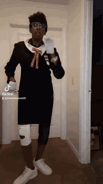 a woman wearing glasses and a black dress is standing in a hallway with a tiktok watermark on the bottom right