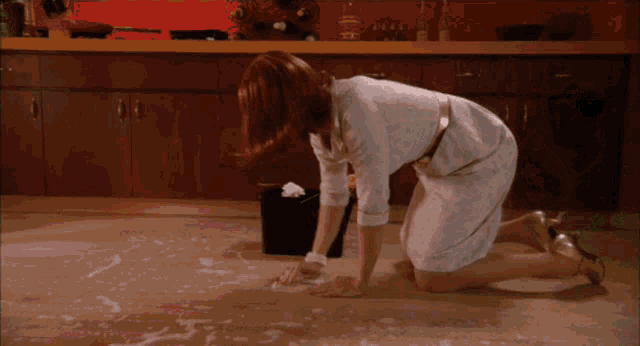 a woman in a white dress is kneeling down to clean the floor