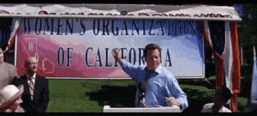 a man is giving a speech in front of a women 's organization of california sign