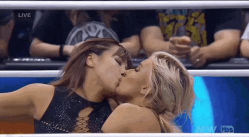 two women are kissing in a boxing ring while a crowd watches .