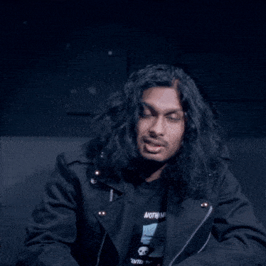 a man with long hair is wearing a black shirt that says " vote "