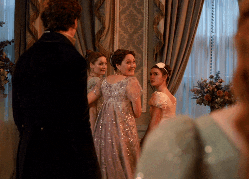 a group of women are standing in a room with a man standing in the background