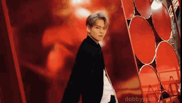 a man in a black suit is standing in front of a red wall with circles on it .