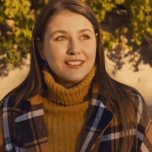 a woman wearing a plaid jacket and a turtleneck sweater smiles