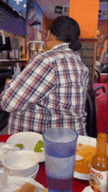 a woman in a plaid shirt sits at a table in front of a bottle of salsa