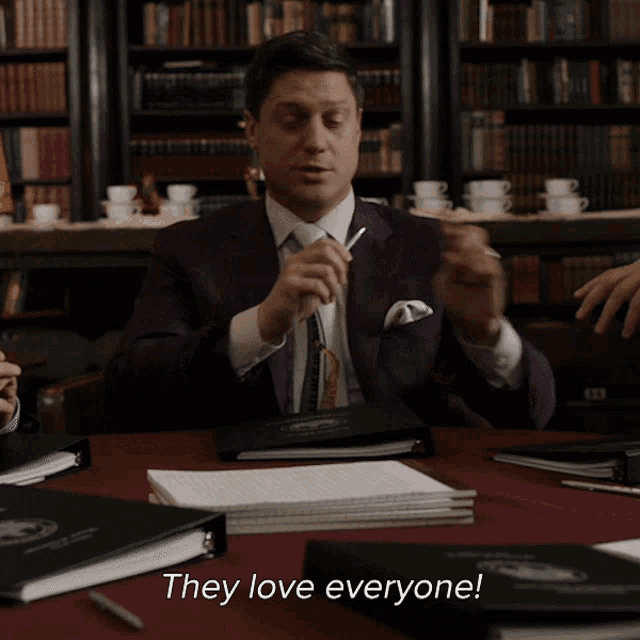 a man in a suit and tie is sitting at a table with the words they love everyone on the table