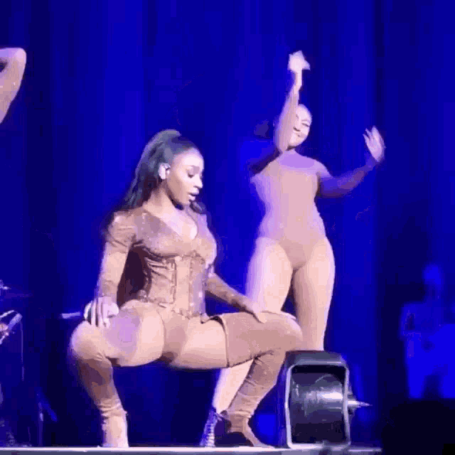 two women are dancing on a stage with a blue background .