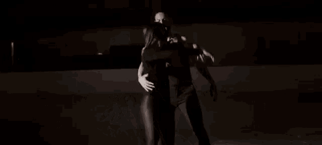 a man is holding a woman in his arms while they are dancing in the dark .