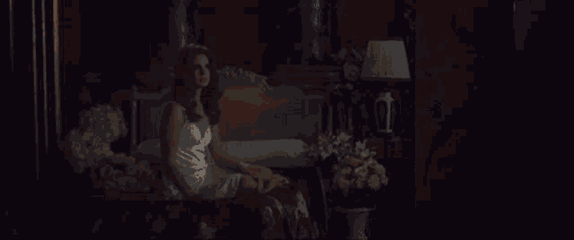 a woman in a white dress is sitting on a bed with flowers