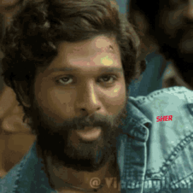 a man with a beard is wearing a denim jacket and looking at the camera .