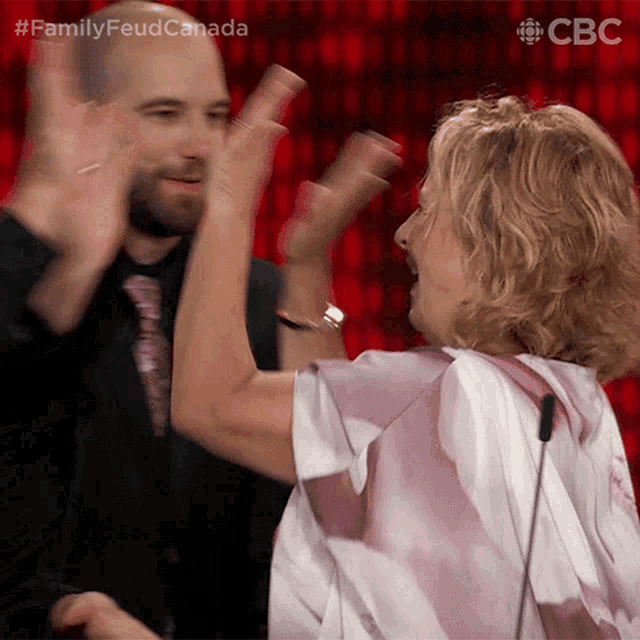 a man and a woman are giving each other a high five in front of a screen that says family feud canada