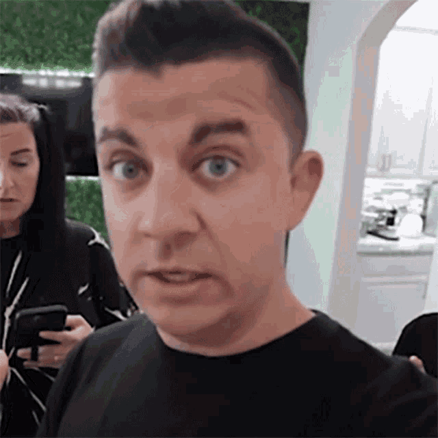 a man in a black shirt is making a funny face while holding a cell phone