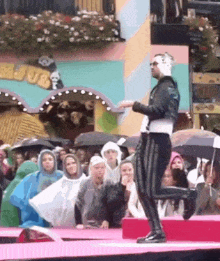 a man is standing on a stage in front of a crowd with umbrellas in front of a building that has the word pub
