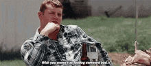 a man in a plaid shirt is sitting at a table with a bottle of beer in front of him .