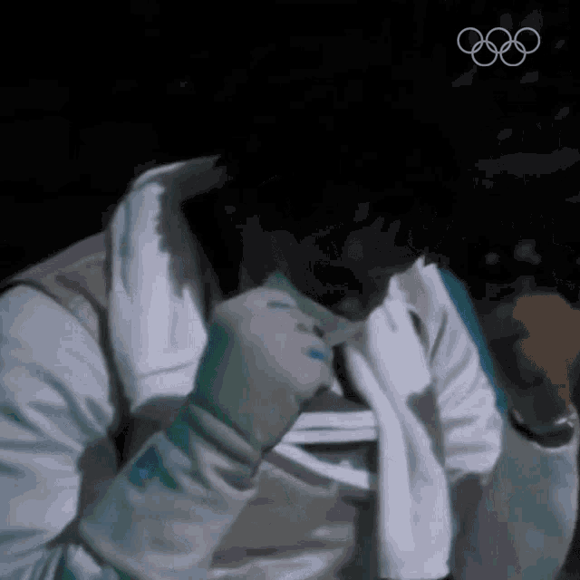 a fencer wipes his face with a towel while wearing a white vest and gloves