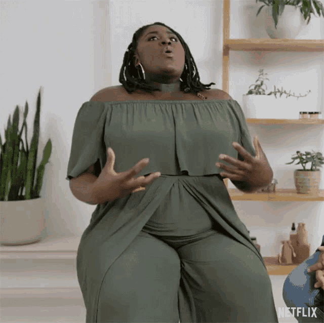 a woman in a green dress is sitting in front of a shelf that says netflix on it