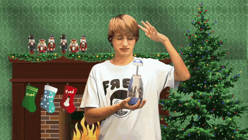 a boy wearing a white shirt with the word fred on it stands in front of a christmas tree