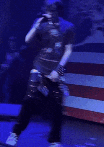 a man is dancing in front of an american flag while wearing a blue shirt