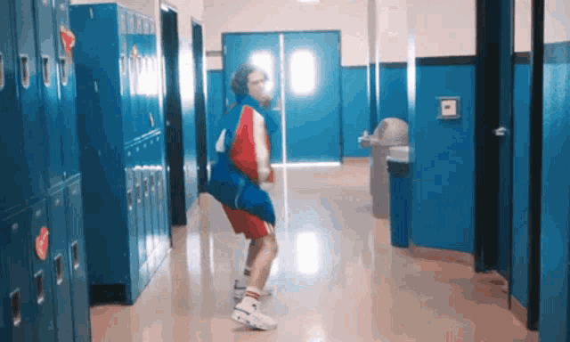 a person is dancing in a hallway with blue lockers .
