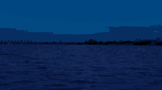 a dark blue water surface with trees in the background