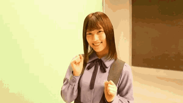 a young woman wearing a purple shirt and a black bow tie is standing in front of a green wall .