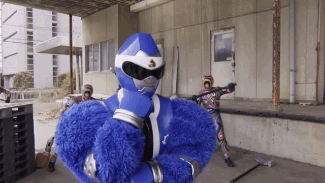 a blue superhero is standing in front of a building with another superhero holding a gun