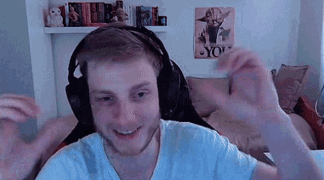 a man wearing headphones and a white shirt is sitting in front of a poster of yoda .