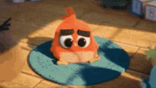 a red angry bird is sitting on a blue rug on the floor .