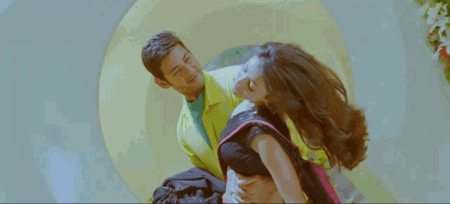 a man in a yellow jacket is holding a woman in a black and pink saree