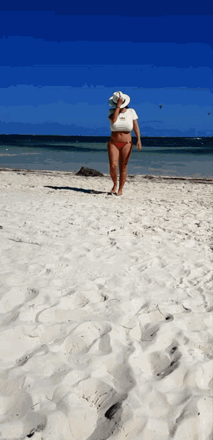 a woman wearing a red bikini and a white hat walking on a beach