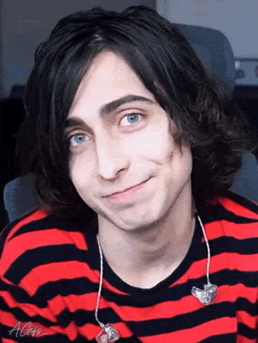 a young man with blue eyes is wearing a red and black striped shirt and ear buds