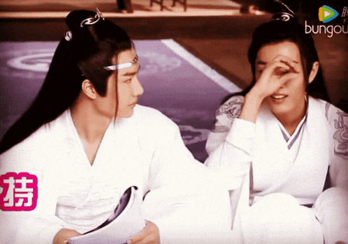 two men are sitting next to each other and one is covering his face