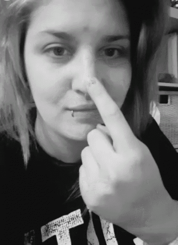 a woman wearing a black shirt with the letter t on it touches her nose
