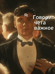 a man in a tuxedo and bow tie is standing in a crowd of people with russian writing behind him