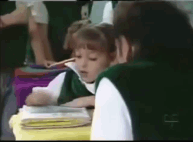 a girl in a green vest sits at a desk with a stack of books