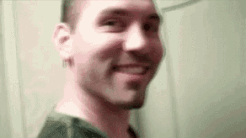 a man with a beard is smiling and looking at the camera in a bathroom .