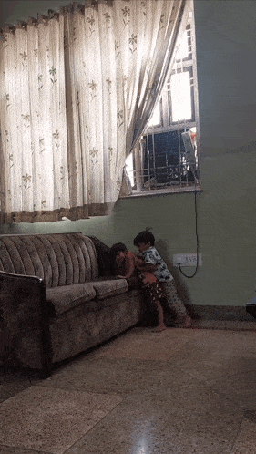 two children are playing on a couch in front of a window with a t.c.a. sticker on the wall