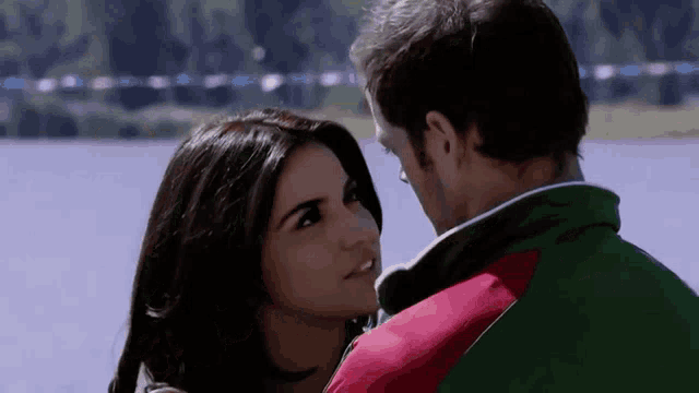 a man and a woman are looking into each other 's eyes in front of a body of water