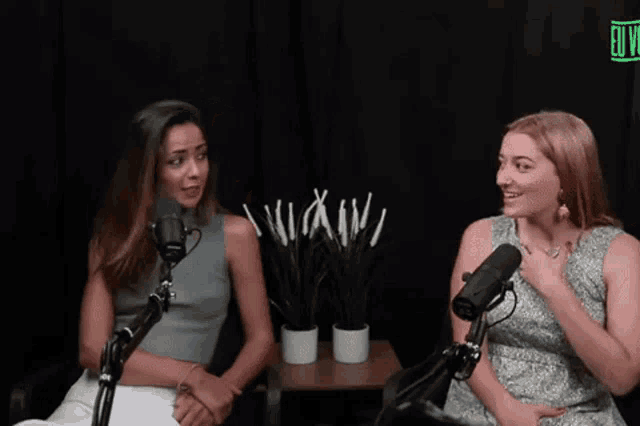 two women are sitting in front of microphones talking to each other in a studio .