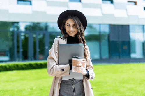 a woman in a hat holds a cup of coffee and a laptop