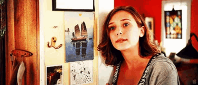 a woman is leaning against a wall with a painting of a boat on it .