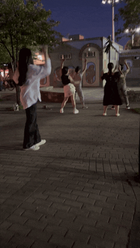 a group of people dancing on a brick sidewalk at night