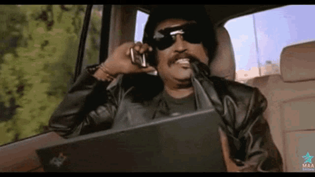 a man wearing sunglasses is talking on a cell phone while sitting in a car with a laptop