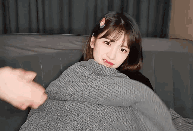 a girl is sitting on a couch covered in a blanket and a person is putting a blanket on her .