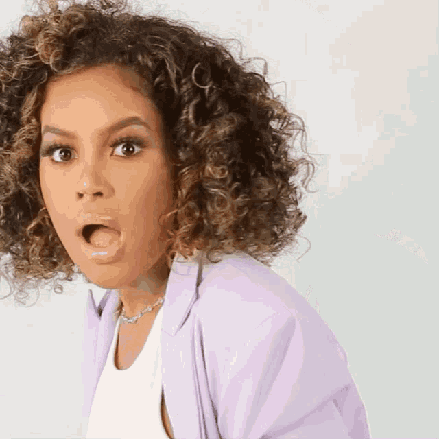 a woman with curly hair is wearing a purple jacket and a white shirt